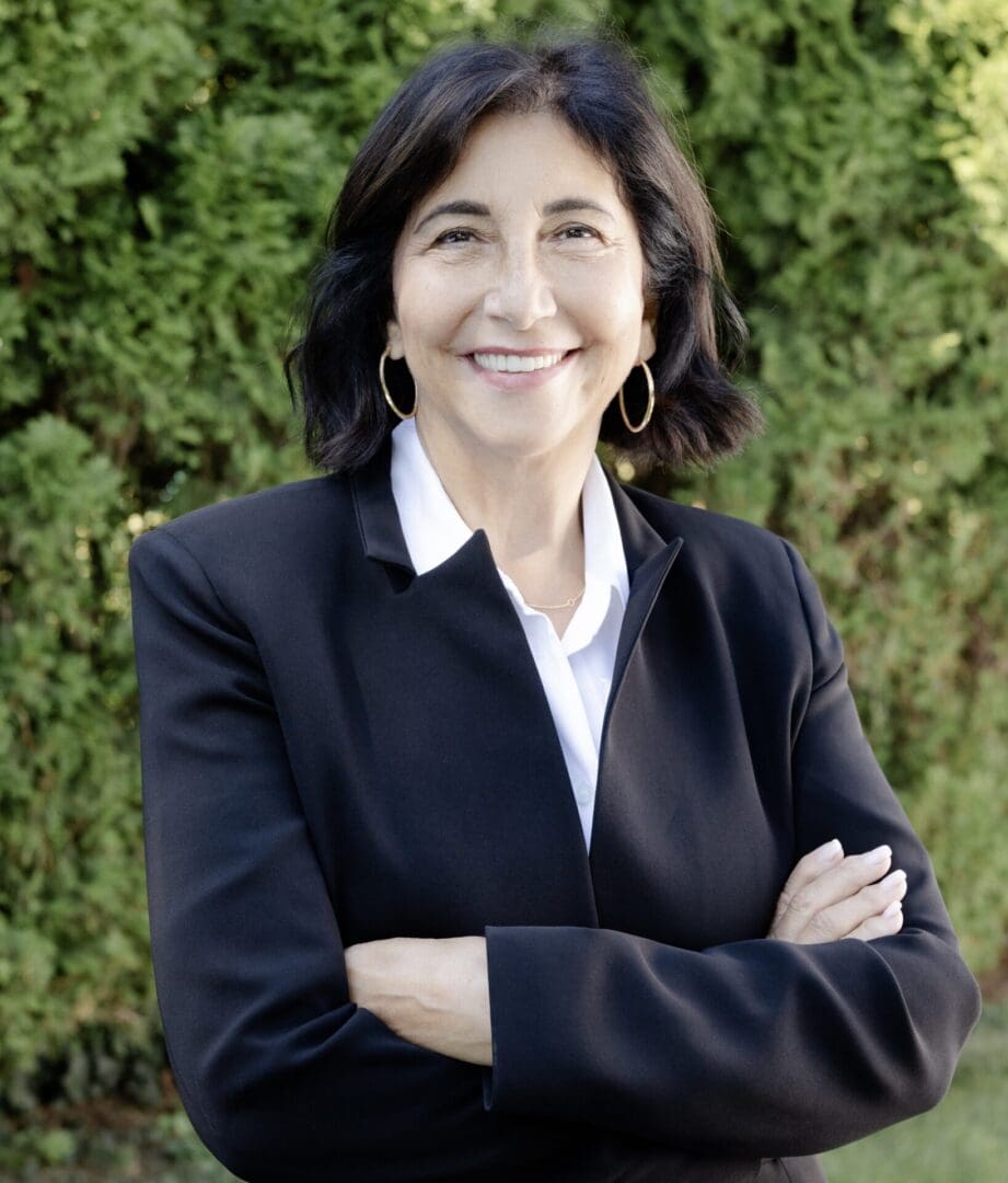 Smiling person in black suit, outdoor background.
