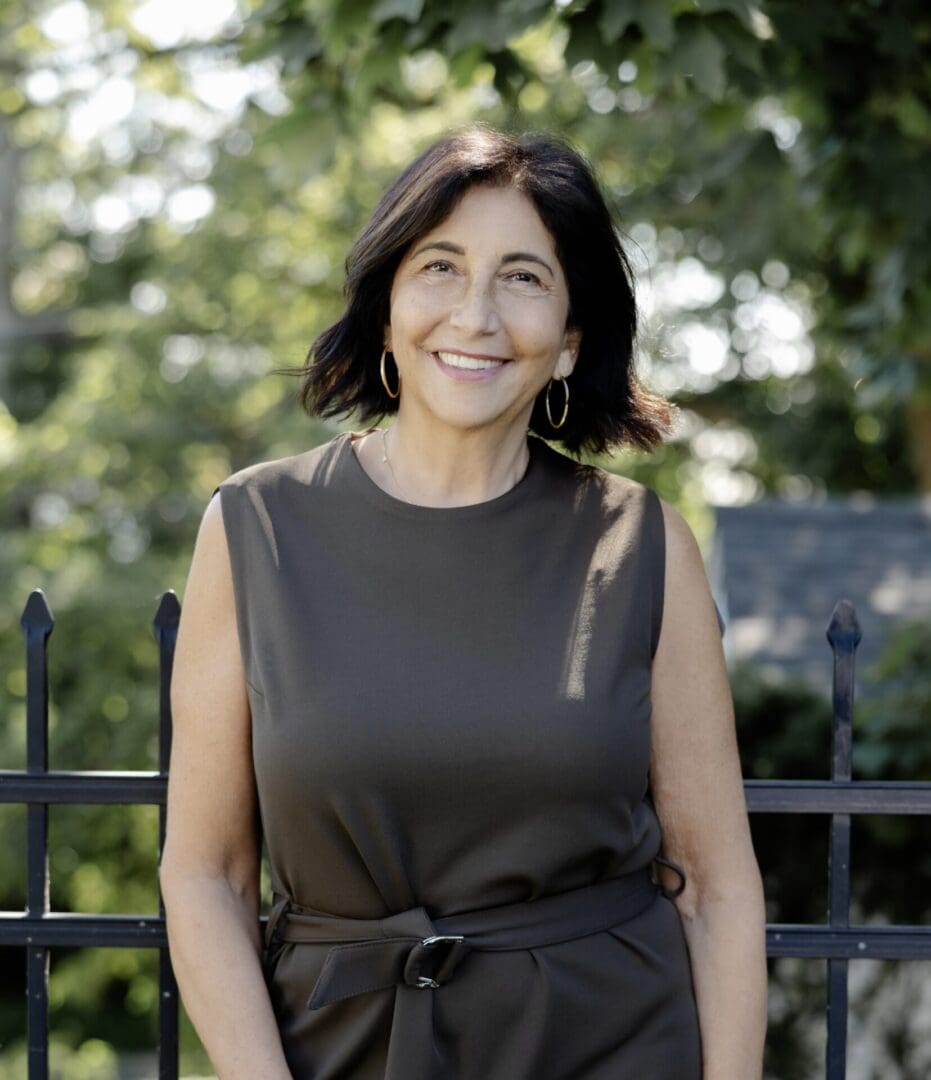 Smiling woman standing outdoors near wrought iron fence.