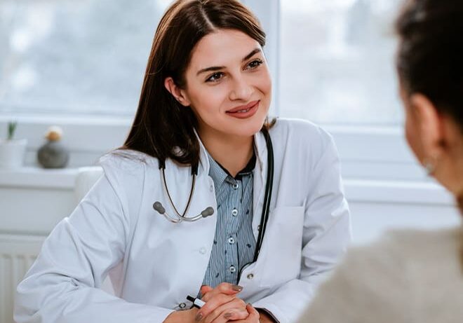 A woman in white coat sitting at table with another person.