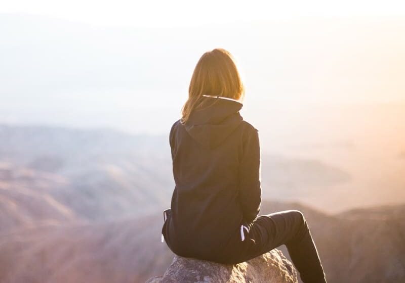 Woman sitting on a cliff overlooking a valley.