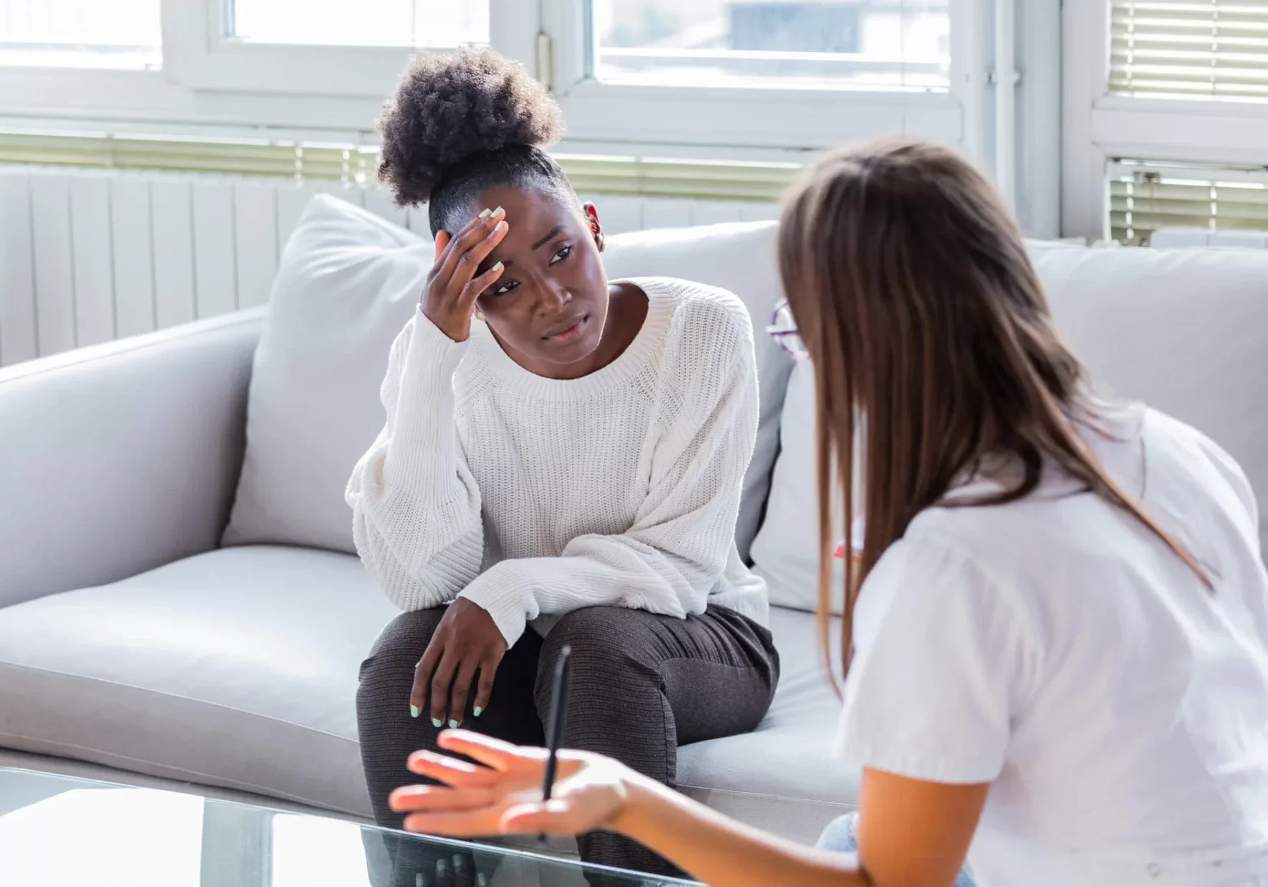 Two women sitting on a couch talking to each other.