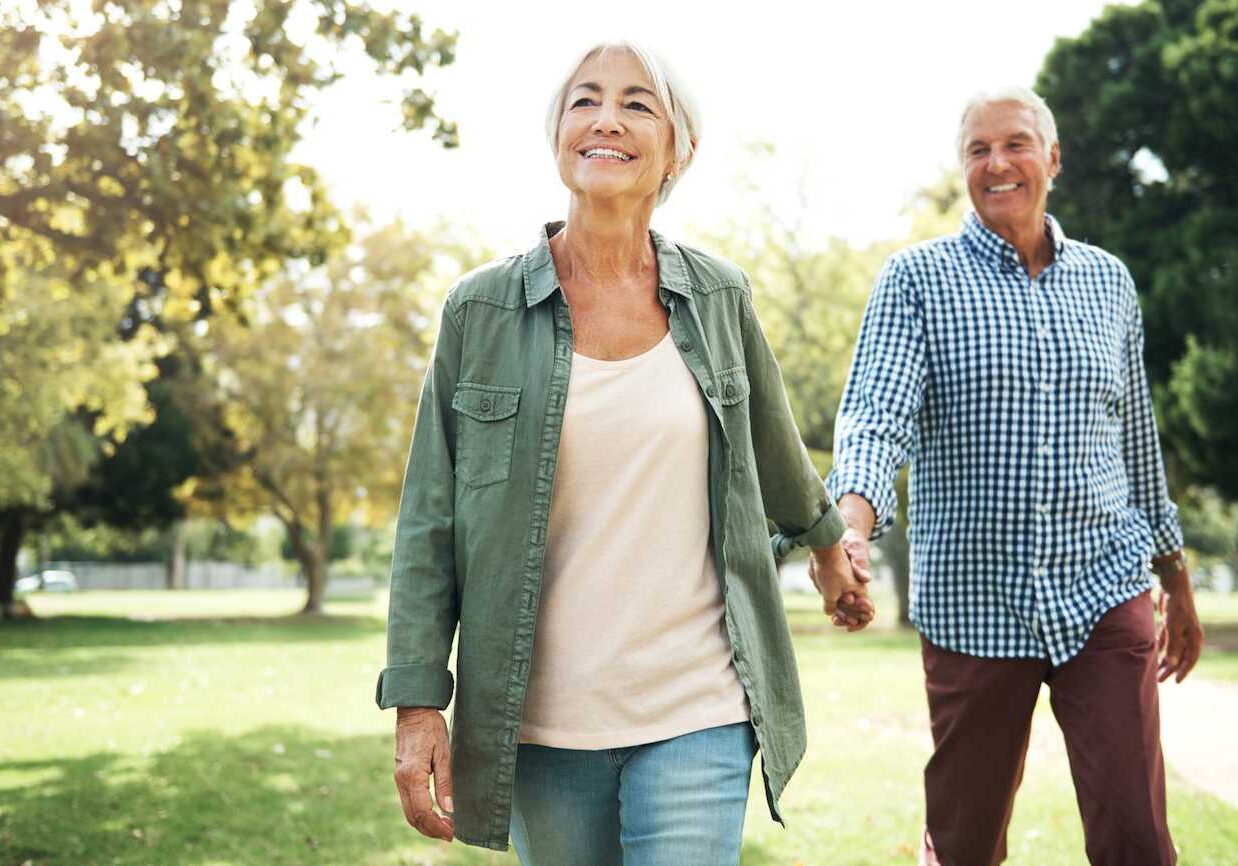 A man and woman walking in the park holding hands.